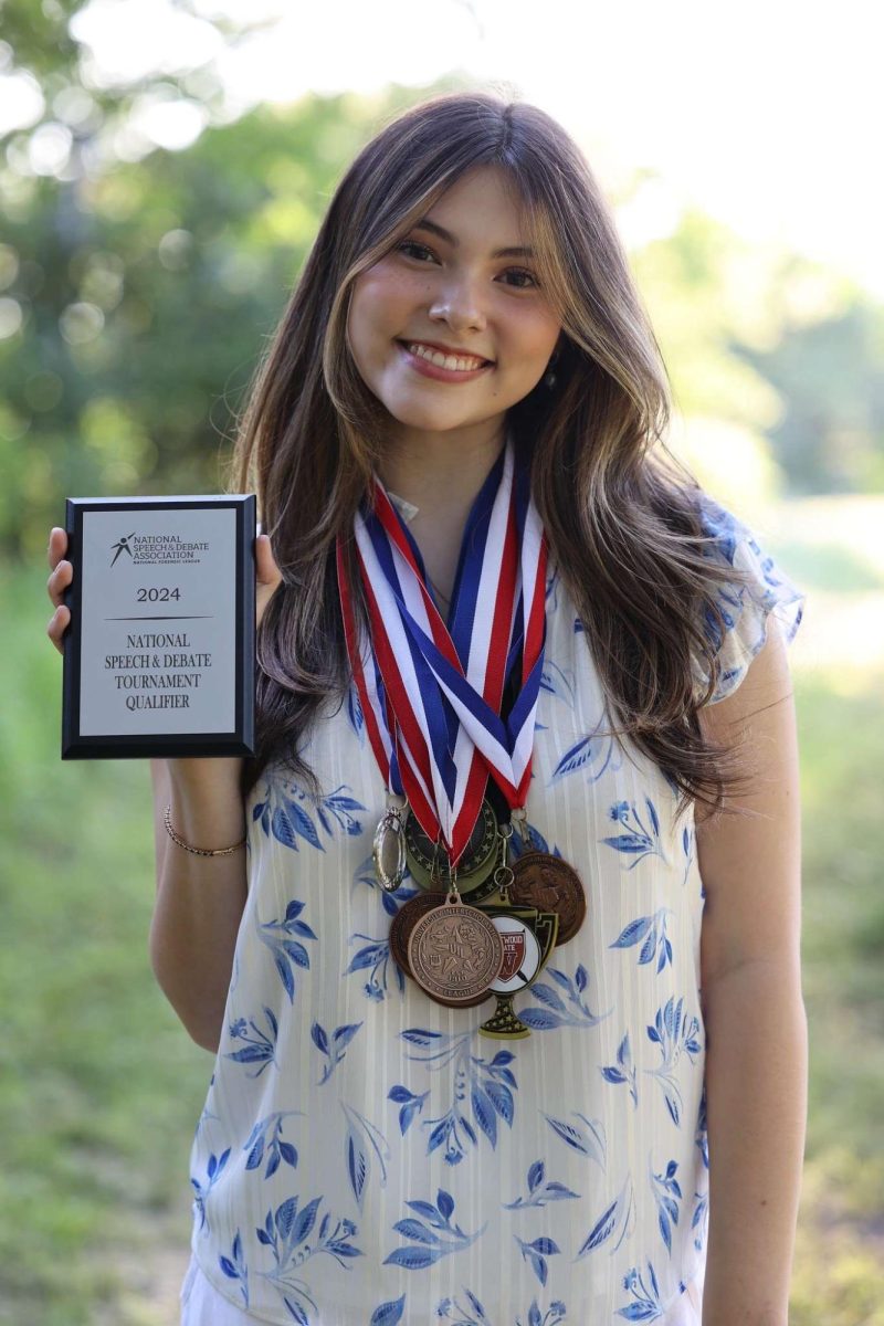 Weighed down by her speech medals, senior Kendall Trujillo shows off her NSDA Nationals plaque in her senior photoshoot. “I’m most looking forward to performing in front of people whove never seen my speech before,” Trujillo said. “I can’t wait to watch the other competitors too.”